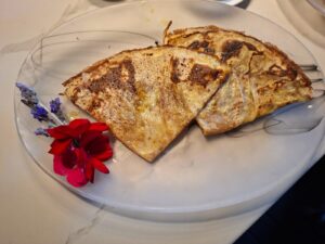 Two thin crepes folded into triangles on a white plate with a red flower and sprig of lavender